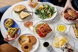Assorted delicious food items on a table including burgers, sandwiches, salad, fries, and drinks at a restaurant